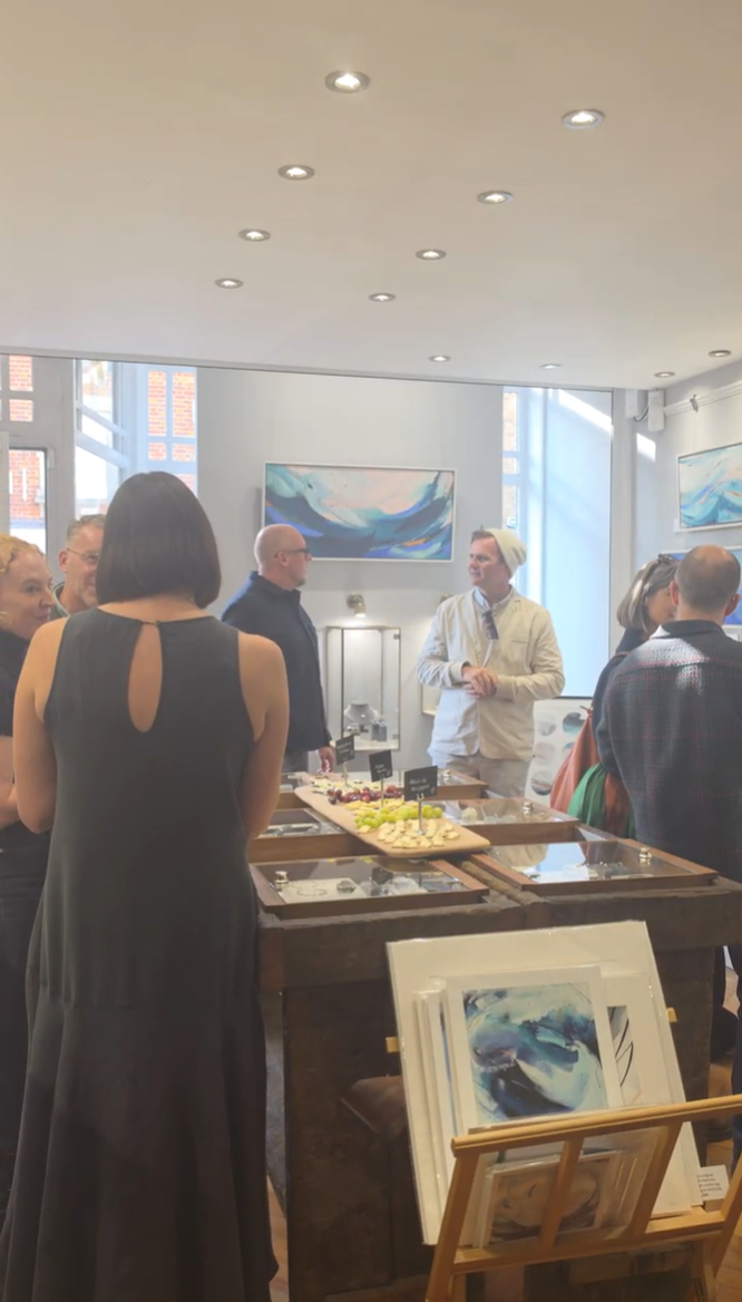 Visitors chatting at KATA Jewellery's Meet the Artist event, surrounded by abstract seascape paintings.